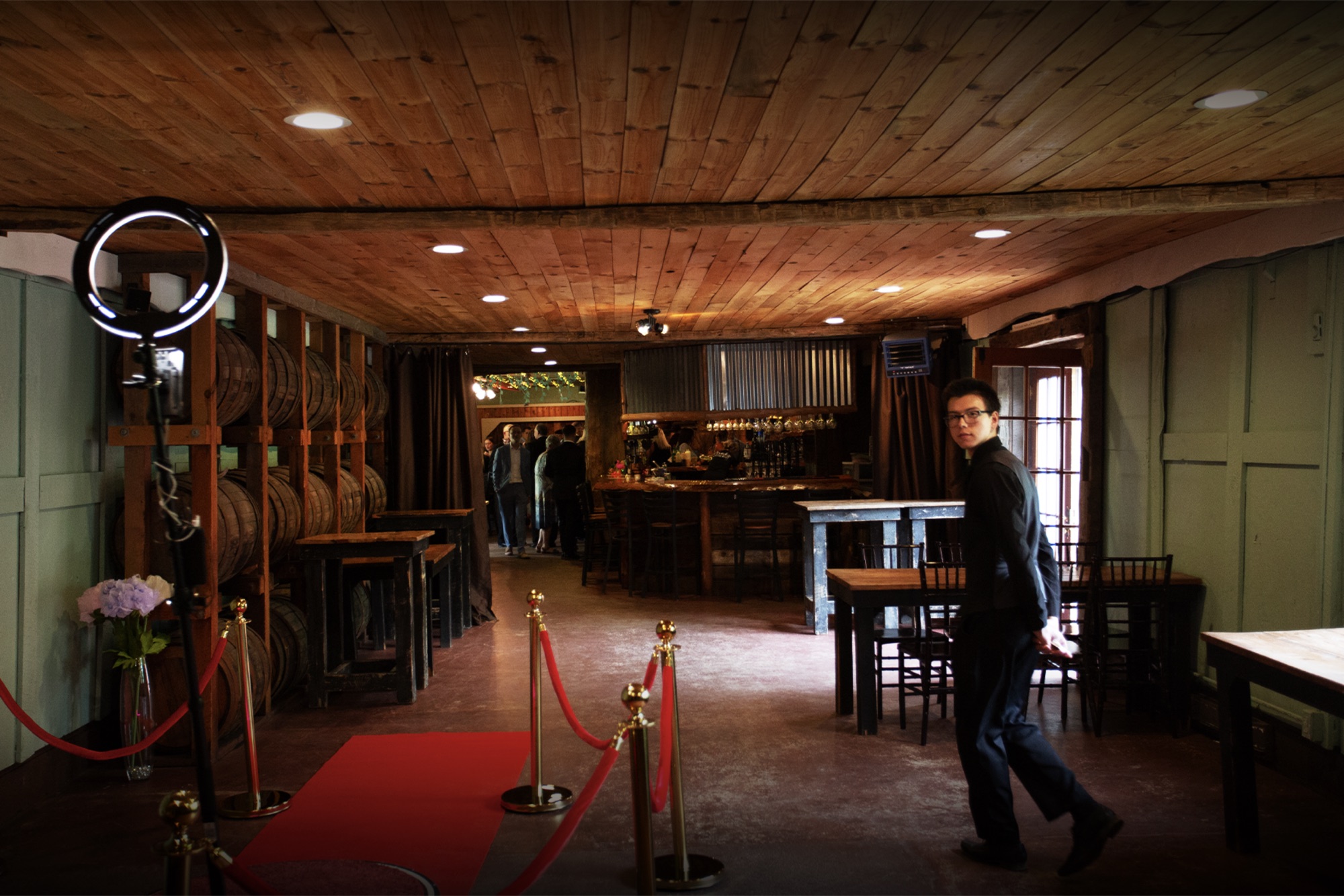 Wide view of the NextSpin 360 booth setup at a barn wedding venue with bourbon barrels, ring light, red carpet, and velvet rope stanchions.